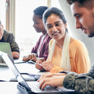 Four international students on laptops sitting at a classroom table working on assignments for their interdisciplinary studies at their US university