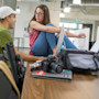 Two male college students sit across from a female college student sitting on a long table in front of a camera and a laptop at the University of Utah Lassonde Center