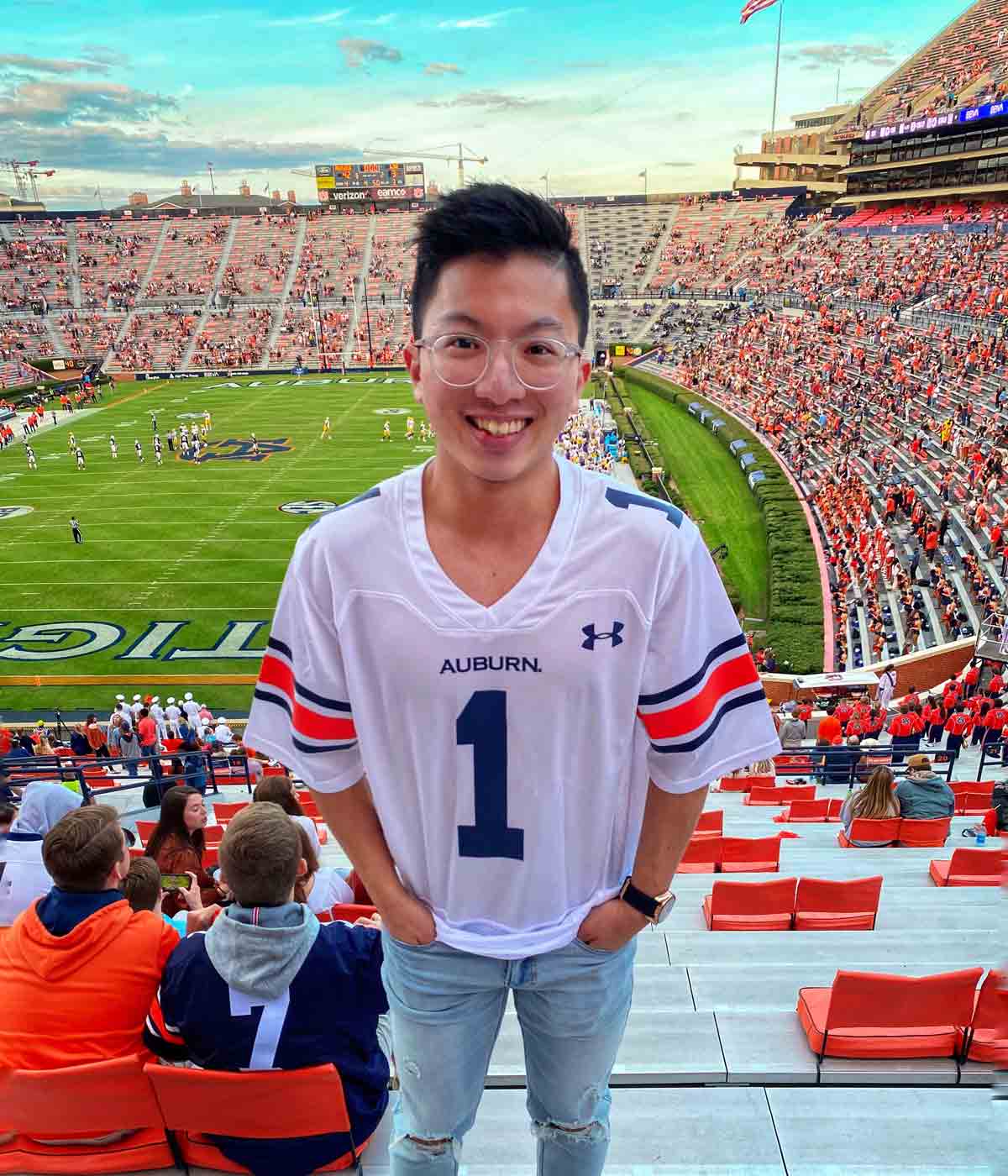Justin, an Auburn University international student from Taiwan, stands in the stadium at an Auburn football game and smiles for the camera
