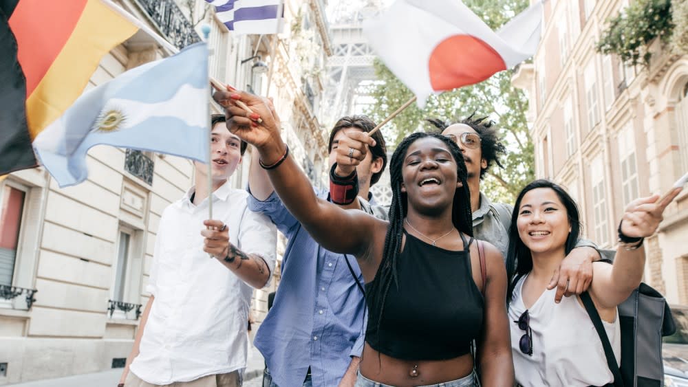 A group of international students walk together on a US college campus and wave flags from many nations