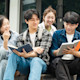 Four international students from Indonesia sit on the steps of their US university library and work on an assignment together.