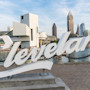 The Cleveland Script sign sculpture at Edgewater Park is in the foreground of this image, the Cleveland skyline and Cuyahoga River is in the background.