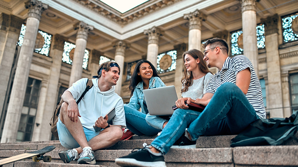 A group of international students sit outside on the steps of a campus building at their US university.