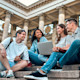 A group of international students sit outside on the steps of a campus building at their US university.