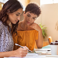 A female international student sits next to her mother and they look over a notebook and US university bill