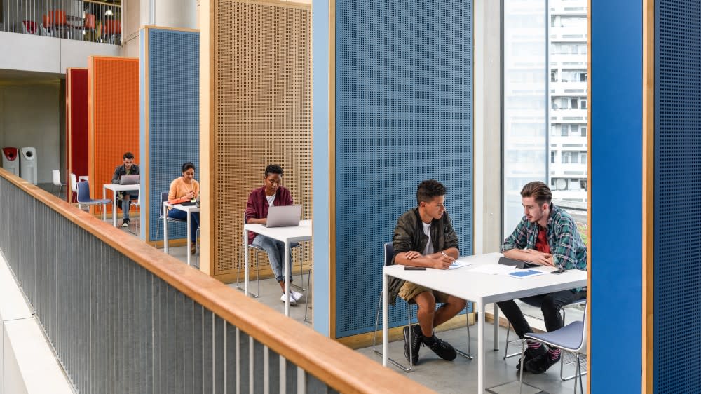 After planning to take the English language test for international students to study in the US, five international students sit at tables behind partitions and study for the English exam for USA.