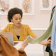 In a fashion design course, two fashion design students in the US sit at a table with laptops next to a rack of clothes. Take classes for fashion at US universities with Shorelight.