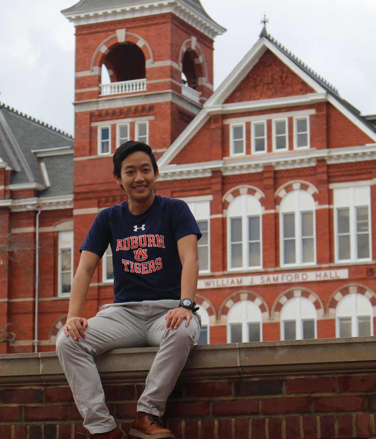 Natcha, an international student from Thailand studying civil engineering, sits on a brick wall on the Auburn University campus