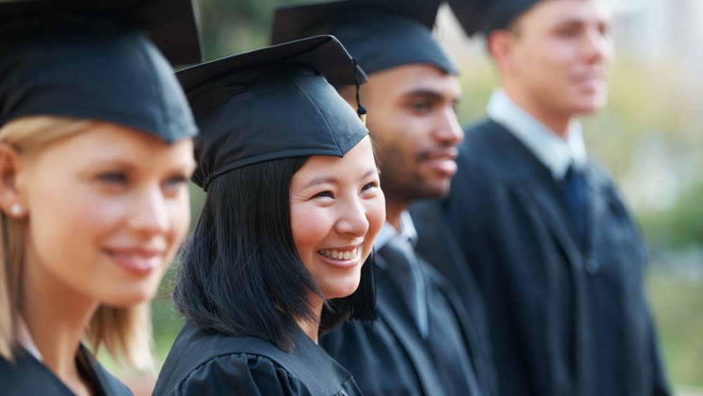 A female international student from Asia wearing a cap and gown stands among fellow graduates on her graduation day at a US university