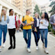 A group of international students holding textbooks walk and laugh together on a city campus
