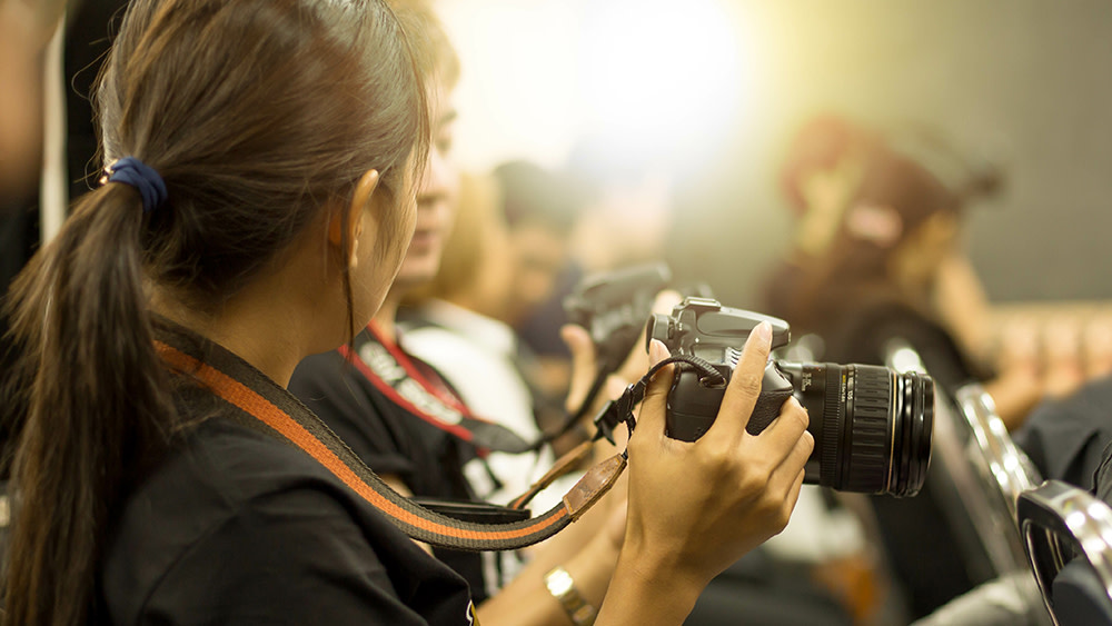 Two international students majoring in journalism at their US university are seen in profile holding professional cameras.