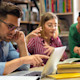 A group of three Canadian students sit at a table with laptops preparing their student visa USA from Canada.