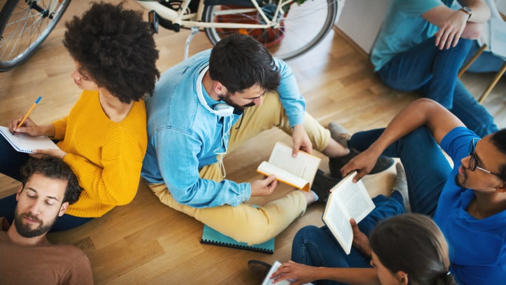 A small college study group sits on the floor each holding open the book being discussed.