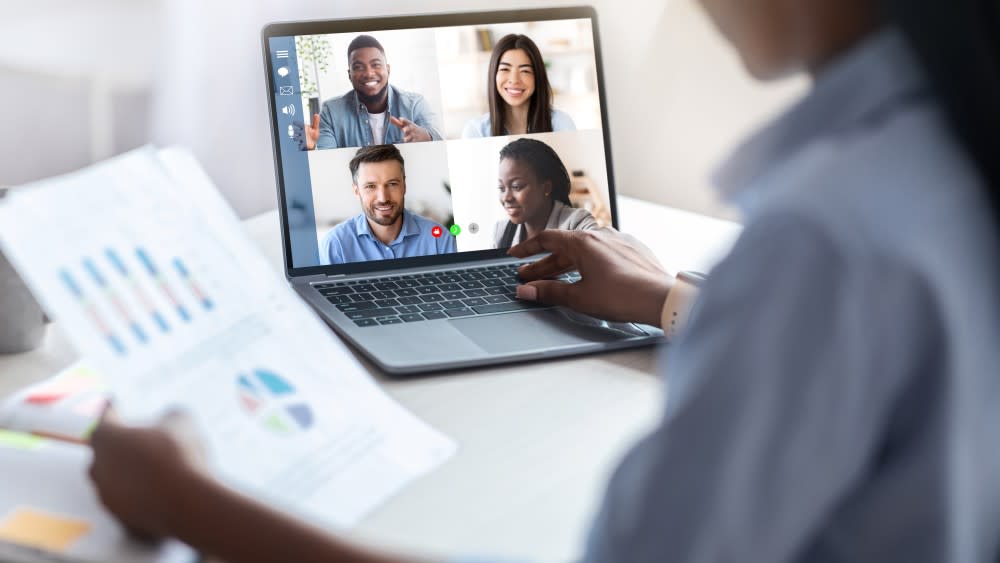 An open laptop on a desk shows four colleagues on a videoconference speaking to an international student during their online internship