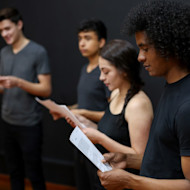 What are electives? Electives are courses at US universities that count toward graduation but may not be directly related to a student's major or degree program. In this image, a group of three international students taking an elective course at a US university stand in a row and study scripts for a theater exercise.