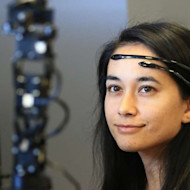 A UDayton female international student engineer sits in front of an AI tower device wearing head gear