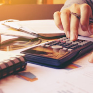 A close up of a finance major student's hand using a calculator with papers underneath. Explore finance majors or what it's like to major in finance at Shorelight universities.