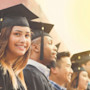 After learning about the American education system, the definition of higher education, and earning their higher ed degree from the US education system, six students wearing graduation caps and gowns stand while a woman in the middle smiles at the camera.