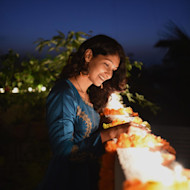 A female South Asian international student stands on a balcony overlooking a ledge filled with lights for Diwali