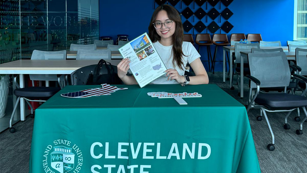 Kate, a Cleveland State Global student ambassador from Vietnam, sits at a table at a university fair and holds up a Cleveland State Global brochure