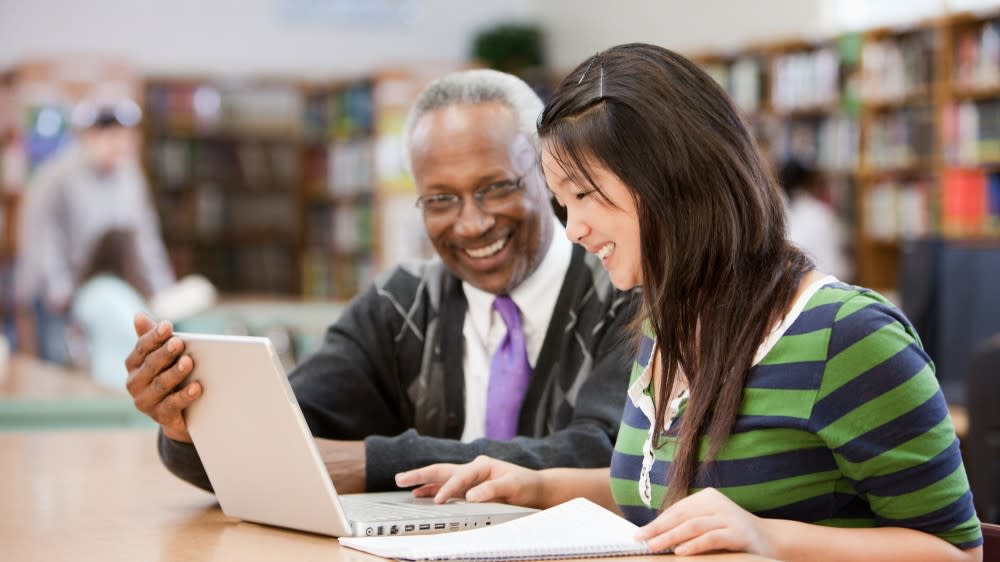 A female international student from Asia sits next to a Black male career coach as they go over her resume in front of a laptop
