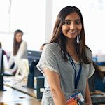 A female international student wearing a lanyard and ID smiles for the camera at her job