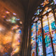 This image shows an oversized stained glass window at a Christian college in the US reflecting colorful sunbeams on an adjacent stone wall.