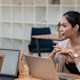 A female international student sits at a table in front of an open laptop and speaks with her education advisor about getting an academic transcript to submit with her US university application.