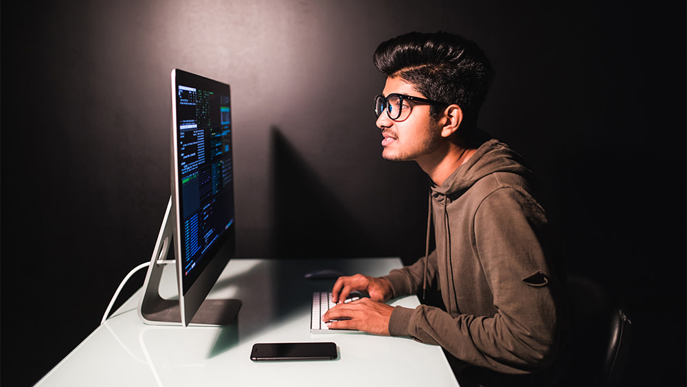 A male international student from South Asia studying to be a data scientist sits at a table and codes for his data science courses. What is data science? Enroll at a US university to pursue a degree in this growing STEM-eligible field.
