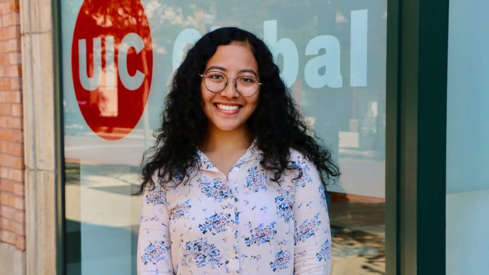 Lila, an international student at the University of Illinois Chicago, smiles at the camera in front of the UIC logo
