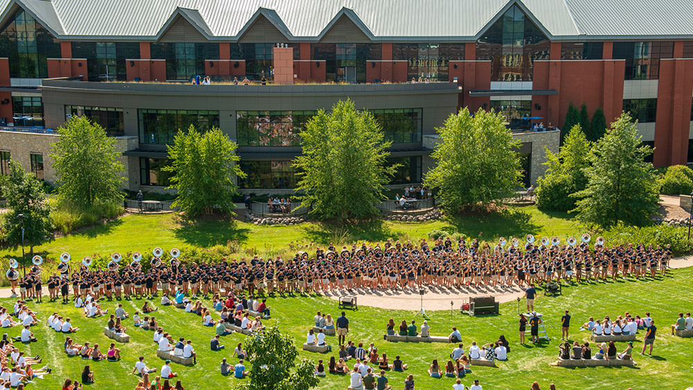 A group of international students visiting from a main campus gather outside a brick academic building on a satellite campus