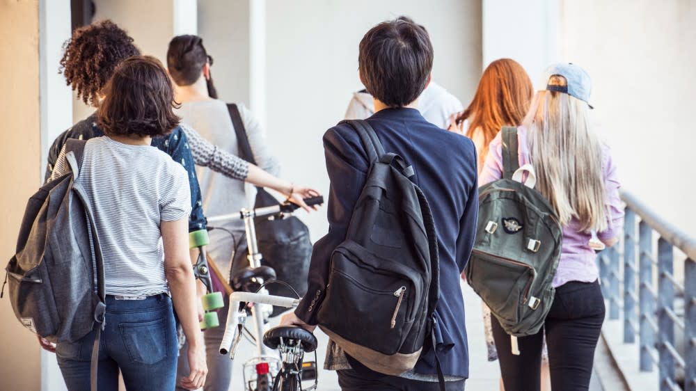 Seen from behind, a group of international students with bikes walk to class past the financial aid for international students office at their US university, which helps with scholarships and how to get student loans.
