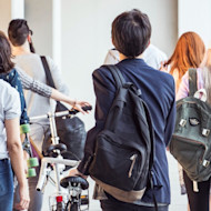 Seen from behind, a group of international students with bikes walk to class past the financial aid for international students office at their US university, which helps with scholarships and how to get student loans.