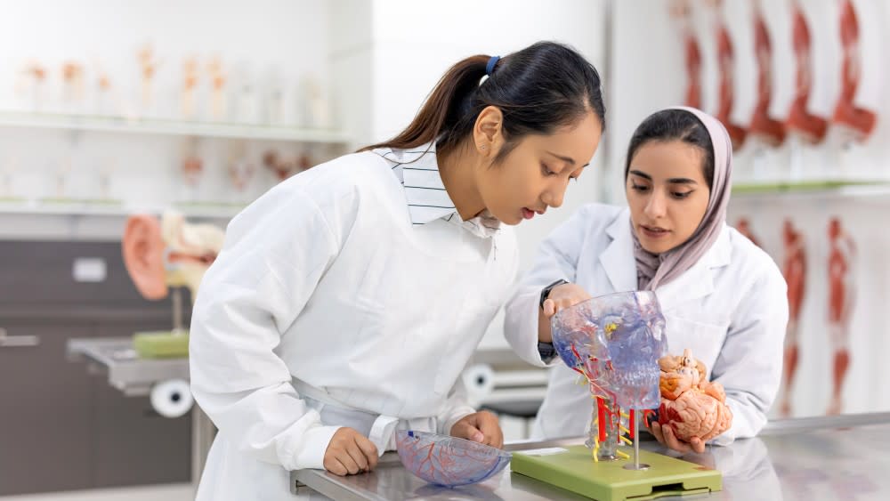 Two female international students in a US university lab look at a petri dish for their biology class