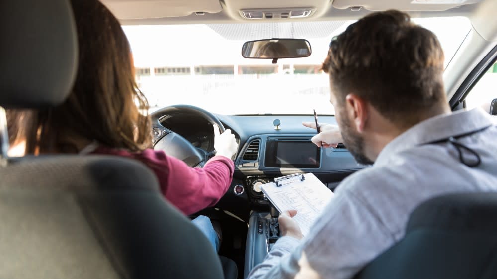 A backseat view of a female student driver with her male driving instructor in the passenger seat.