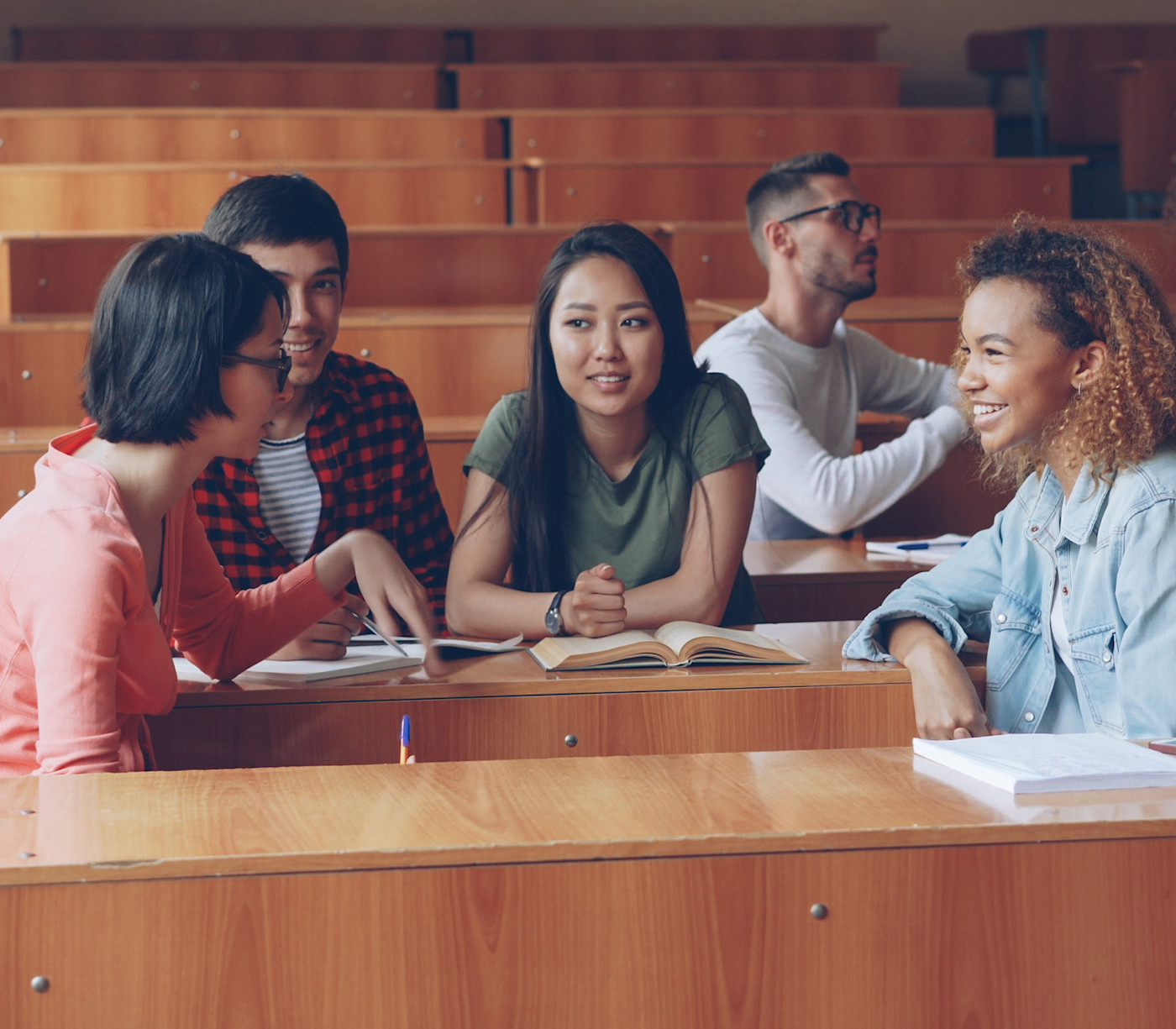 Five international students sit in the auditorium of a US university lecture hall and have a discussion before class.