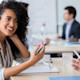 A female international student sits at a table in front of a whiteboard and smiles while holding a pen