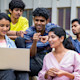 A group of international students from Bangladesh sit outside at their US university and work on a group project together on one laptop.