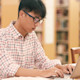 An Asian male international student sits at his laptop in his US university library and works on his dissertation.
