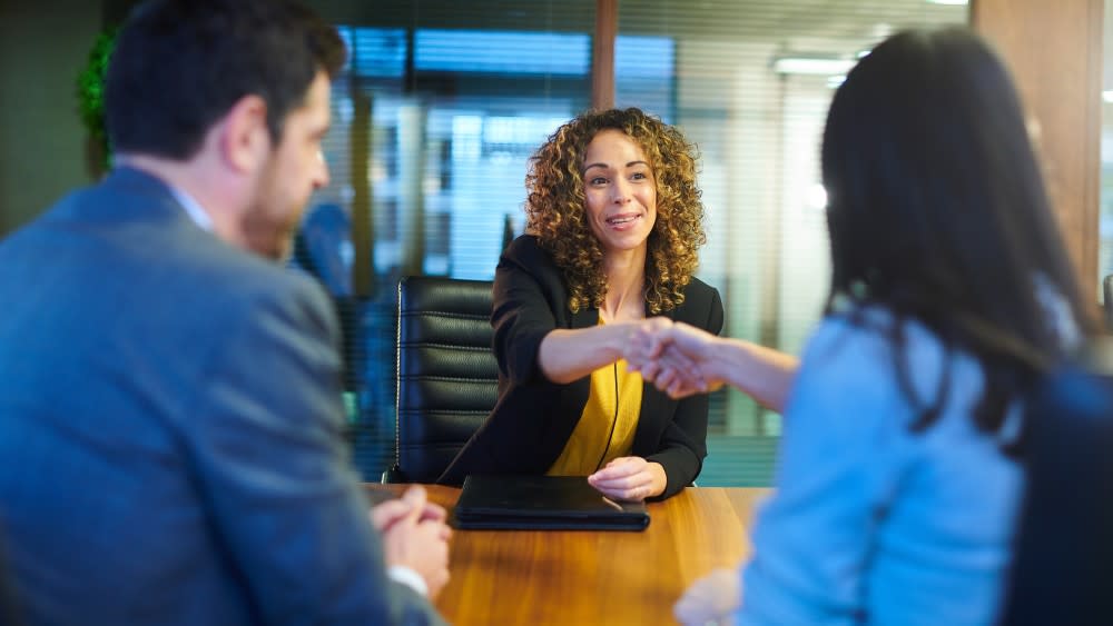 A female international student wearing a suit jacket shakes the hand of a recruiter during an interview for. US job