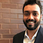 Shrikant from India, an international graduate student at Cleveland State University, smiles while wearing a blazer and stands in front of a brick wall