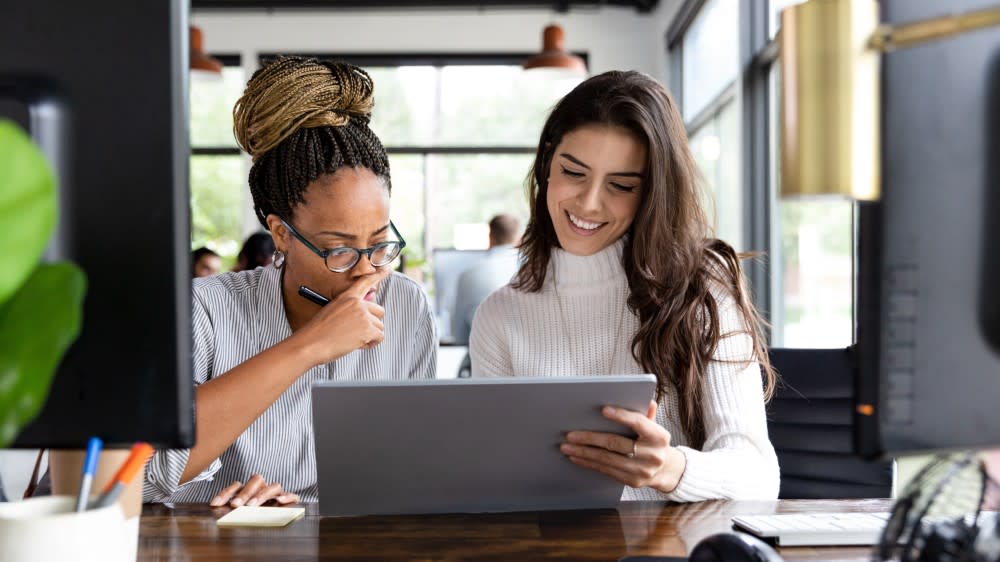 Two female international students sit side by side in front of a laptop