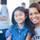 A female college student wearing a "volunteer" t shirt with her arm around a young girl, and both are smiling at the camera.