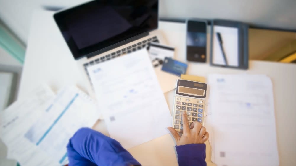 An international student in blue shirt, with only their hands in frame from overhead, calculating their taxes at a table.