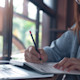 A female international student from Asia sits at her desk with her laptop and day planner and fills out appointments in her US school year calendar.