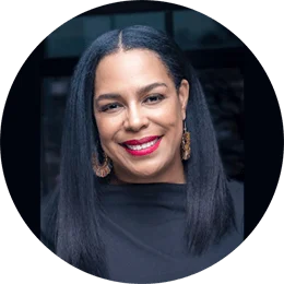 A black woman with long, dark straight hair wears a black blouse and large gold earrings as she smiles at the camera.
