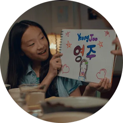 A young Asian girl smiles as she holds up a sign with the American and Korean spellings of her name.