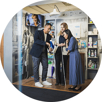 A man holds and points at a bottle of dish soap. Two women stand next to him and lean in to take a closer look.