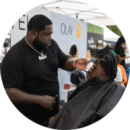 Black consumers experience innovative brands at My Black Is Beautiful, Olay and Bevel stations during the HBCYOU Tour. In the inset, a Black man is seated in a chair and receives a haircut from a barber.