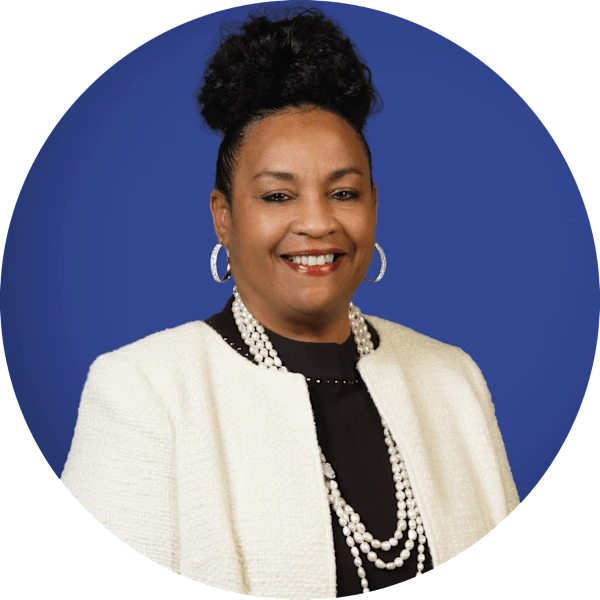A Black woman with dark hair smiles at the camera. She wears a black shirt, white jacket, and pearl necklace.